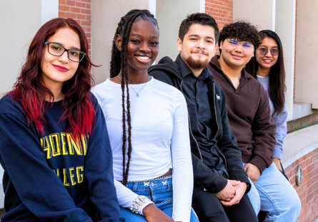 five students sit next to a library smiling