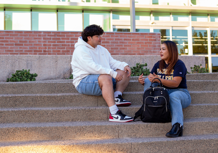 two students sit on steps talking 