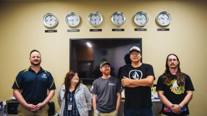 Five veterans gather in Phoenix College's Veteran Services Student Center and stand under six clocks showing the time at various locations around the world. 