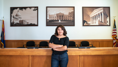 A Phoenix College Paralegal student stands with her arms crossed in front of a courtroom. 