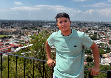 Phoenix College alumnus Luis Herrera leans agains a railing with the sprawl of city visible behind him.  