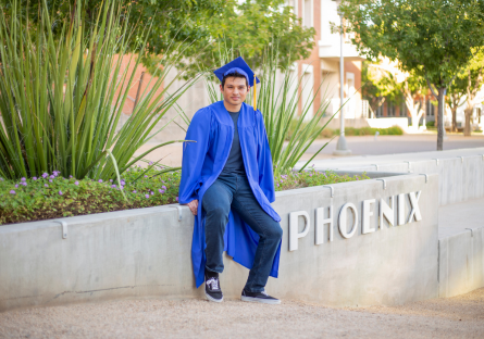 Phoenix College student Elian Jimenez on campus in his blue graduation cap and robe