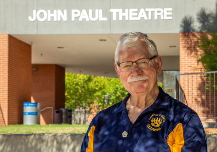 Marty Manning stands in his Phoenix College alumni shirt in front of John Paul Theatre