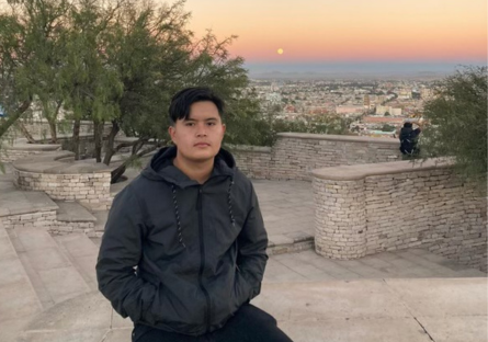 Phoenix College alumnus Luis Herrera sits on a stone wall with a sunset as a backdrop