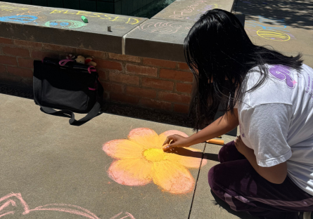 PC student, Jade Trujillo drawing a pink and yellow flower in chalk on Sophomore Square
