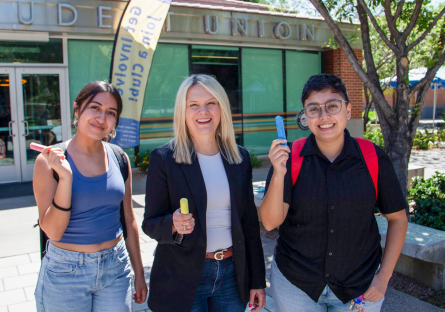 Dr. Kimberly Britt, president of PC, posing with two students in Sophomore Square - they are all holding big colorful pieces of chalk and smiling