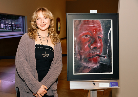 Phoenix College art student Jade Deming stands next to her 2D painting "Up in Smoke," which won a 2025 Vanguard Award 