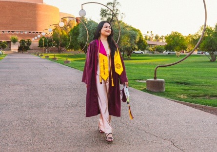 Education major Alejandra Vega at her ASU graduation wearing a grad robe and carrying her cap. 
