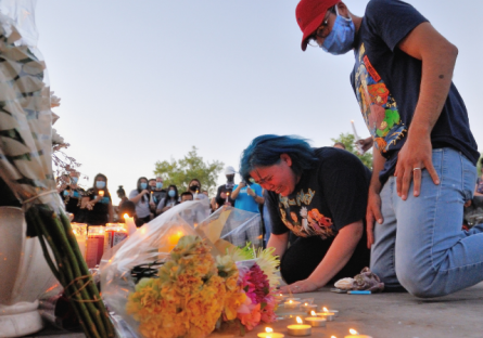 A woman and man kneel before a roadside alter with flowers and candles