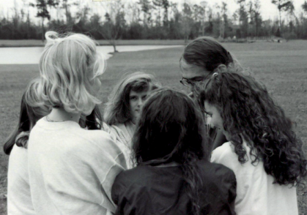 Black and white image of athletes huddled in conversation with their coach