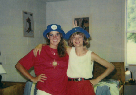 two friends with arms around each other in a college dorm posing for picture