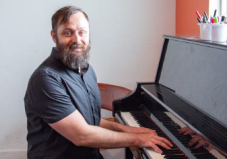 Phoenix College alumnus Jason Mohlenbrock sits at a piano in his youth piano academy, Blue in Green, named after his favorite Miles Davis tune. 