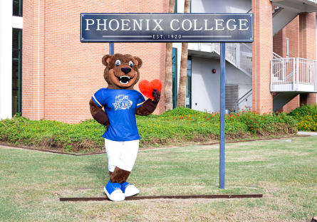 Bumstead (PC Mascot) standing by the Phoenix College Sign holding a red heart